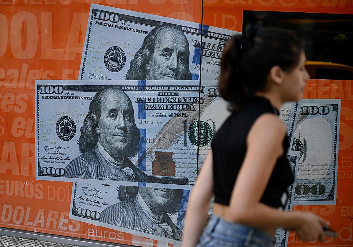 Una mujer pasa junto a una imagen de cien billetes de dólares estadounidenses en Buenos Aires, Argentina