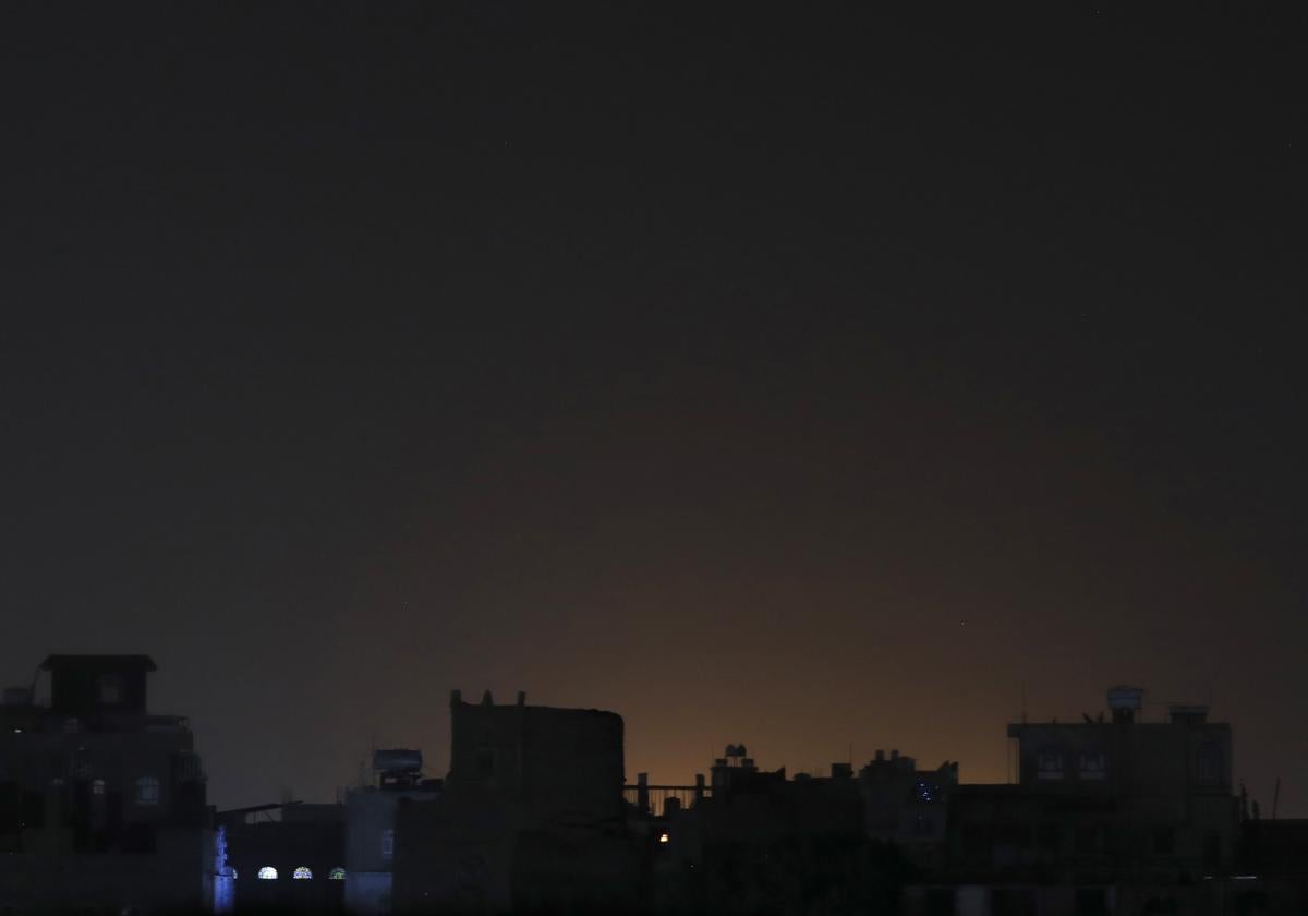 Una vista general de la luz que brilla detrás de los edificios en un vecindario después de los ataques en Sana'a, Yemen