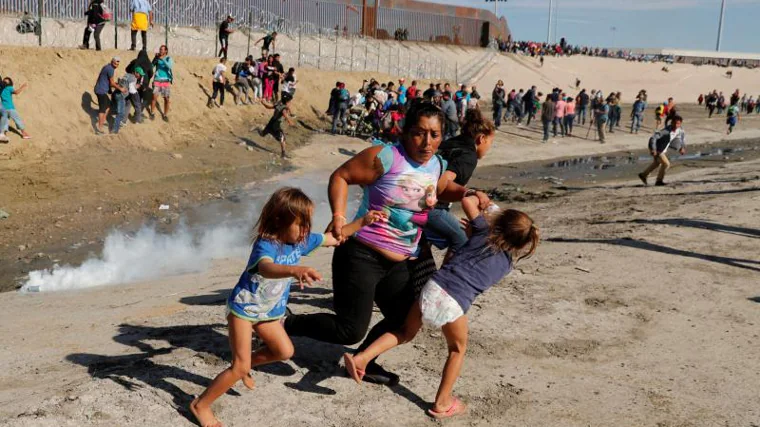 Una familia de migrantes, parte de una caravana de miles de personas que viajan desde Centroamérica rumbo a Estados Unidos, huye de los gases lacrimógenos frente al muro fronterizo entre Estados Unidos y México