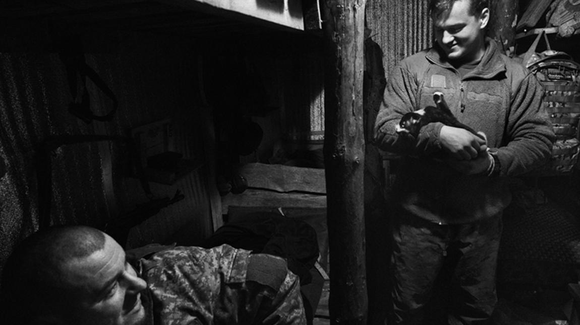Vitaliy y Andriy mientras acaricia su gato conversan bajo la protección de la trinchera de su posición de artillería en el frente de Lyman