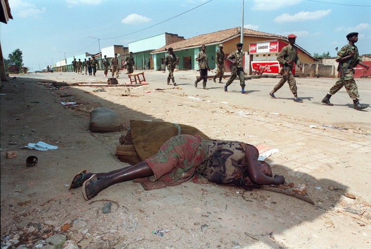 En esta fotografía del 16 de junio de 1994, soldados del Frente Patriótico Ruandés (FPR) caminan junto al cadáver de una mujer asesinada por la milicia progubernamental antes de que la ciudad cayera en manos de los rebeldes
