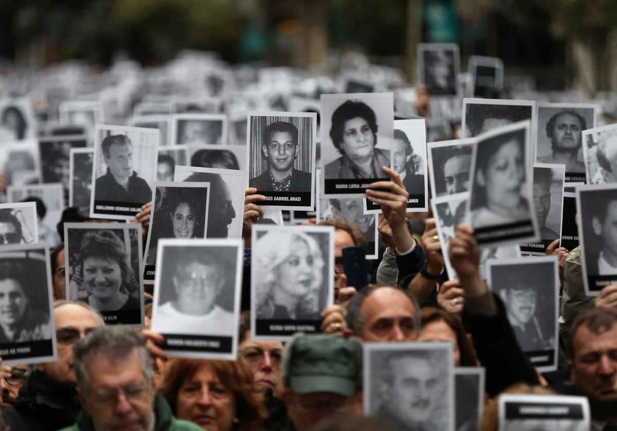 Varias personas sostienen imágenes de las víctimas del atentado de 1994 contra la Asociación Mutual Israelita Argentina (AMIA) en el 25 aniversario