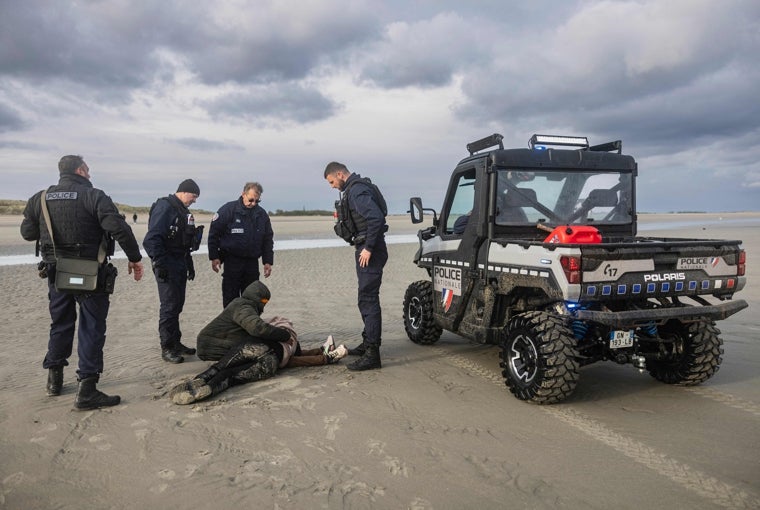 Una pareja de inmigrantes se derrumba junto a agentes de policía franceses después de un intento fallido de cruzar el Canal de la Mancha, en la playa de Gravelines, cerca de Dunkerque