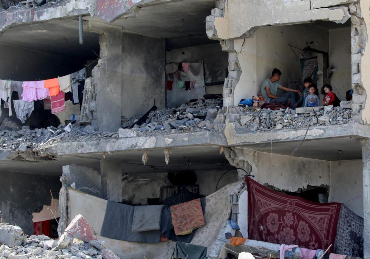 Un palestino y sus hijos sentados en una habitación destruida tras el ataque aéreo israelí contra un edificio residencial en Rafah