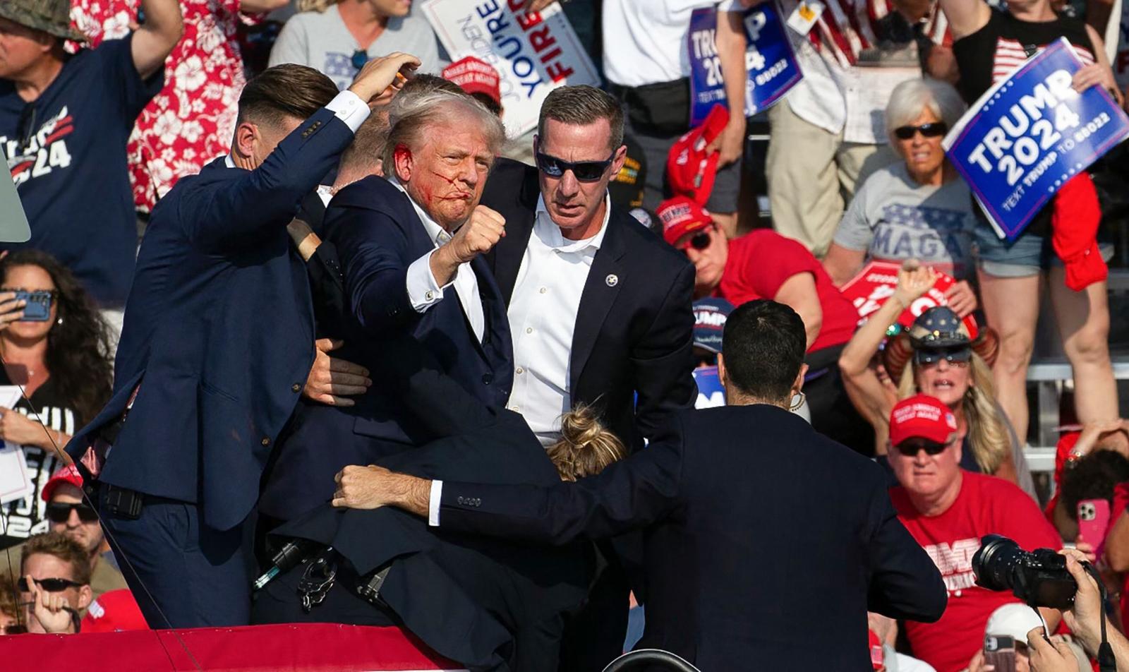 El candidato republicano Donald Trump es visto con sangre en el rostro rodeado de agentes del servicio secreto mientras lo sacan del escenario en un evento de campaña en Butler Farm Show Inc.
