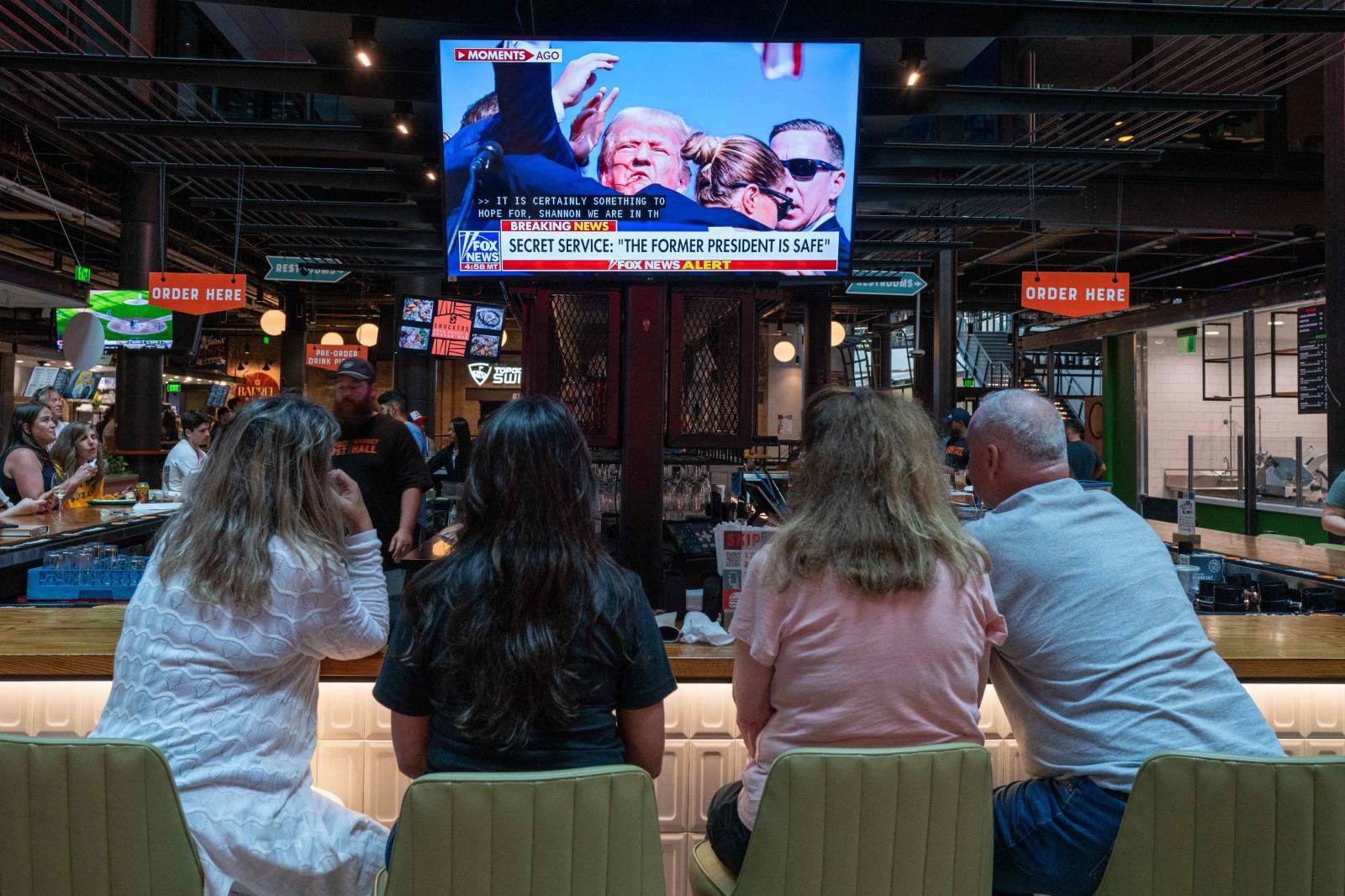 La gente ve las noticias de televisión en un bar de Milwaukee que muestran imágenes de un mitin de campaña del expresidente estadounidense Donald Trump, donde aparentemente resultó herido.