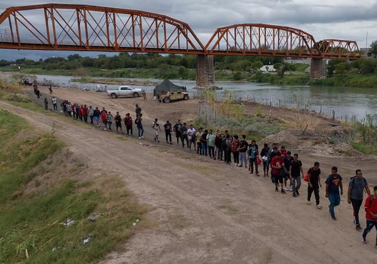 Inmigrantes cruzan el puente negro tras cruzar el Río Grande
