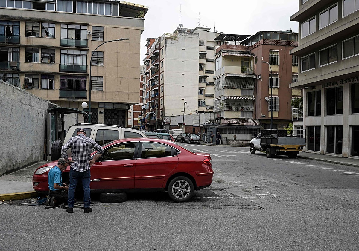 Un hombre trabaja reparando un vehículo mientras su dueño espera en una esquina del barrio Chacao