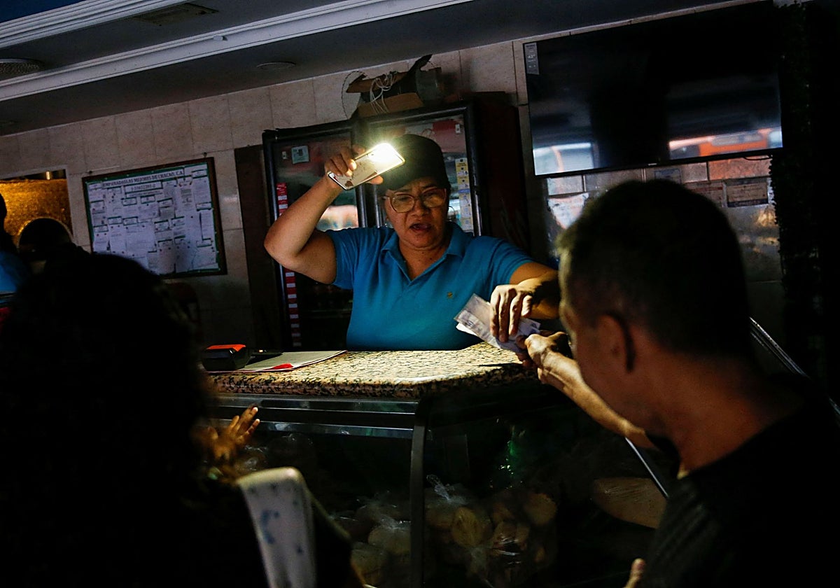 Una mujer recibe dinero en un puesto de comida usando la luz de su teléfono móvil durante un apagón que afecta a Caracas