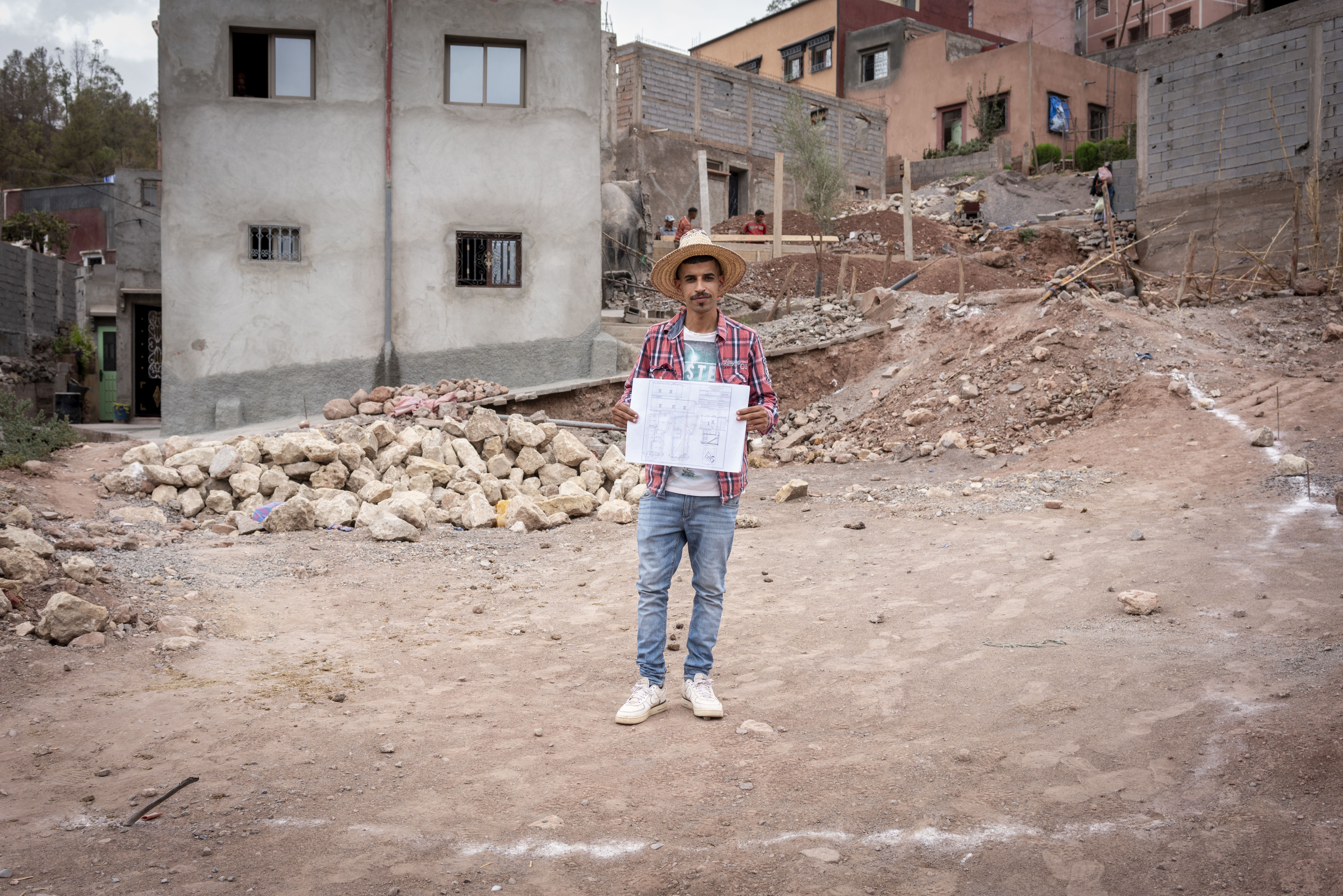 Mouhamed sostiene los planos de su casa en el terreno donde la construirán