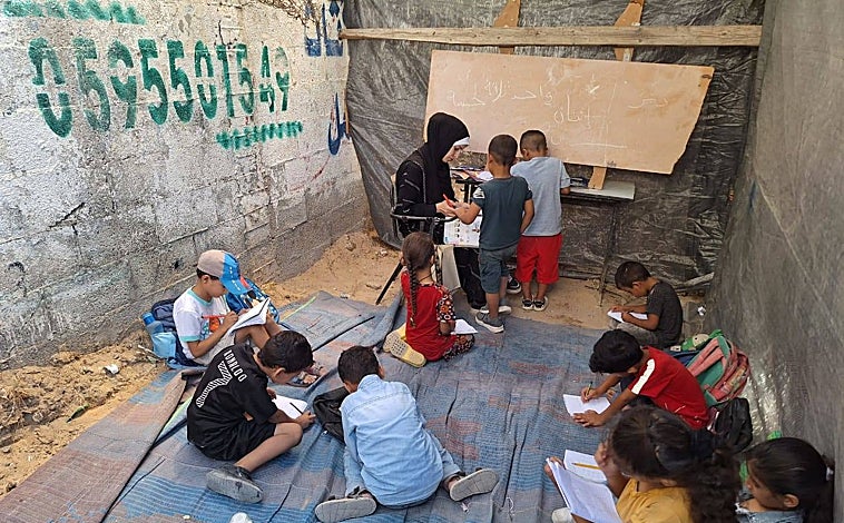 Imagen principal - Desde que empezó la guerra de Gaza en octubre, más del 70 por ciento de las escuelas han resultado destruidas o dañadas. Sin libros, ni lápices, ni pupitres, ni pizarras, los 170 niños que estudian en las aulas improvisadas que dirige la profesora Jaldia al Hasheim intentan no perder su educación, ni su infancia, bajo las bombas del Ejército israelí