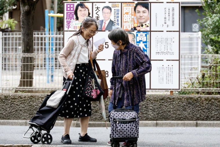 Unas personas caminan delante de un cartel con carteles de campaña de los candidatos que se presentan a las próximas elecciones generales en Tokio