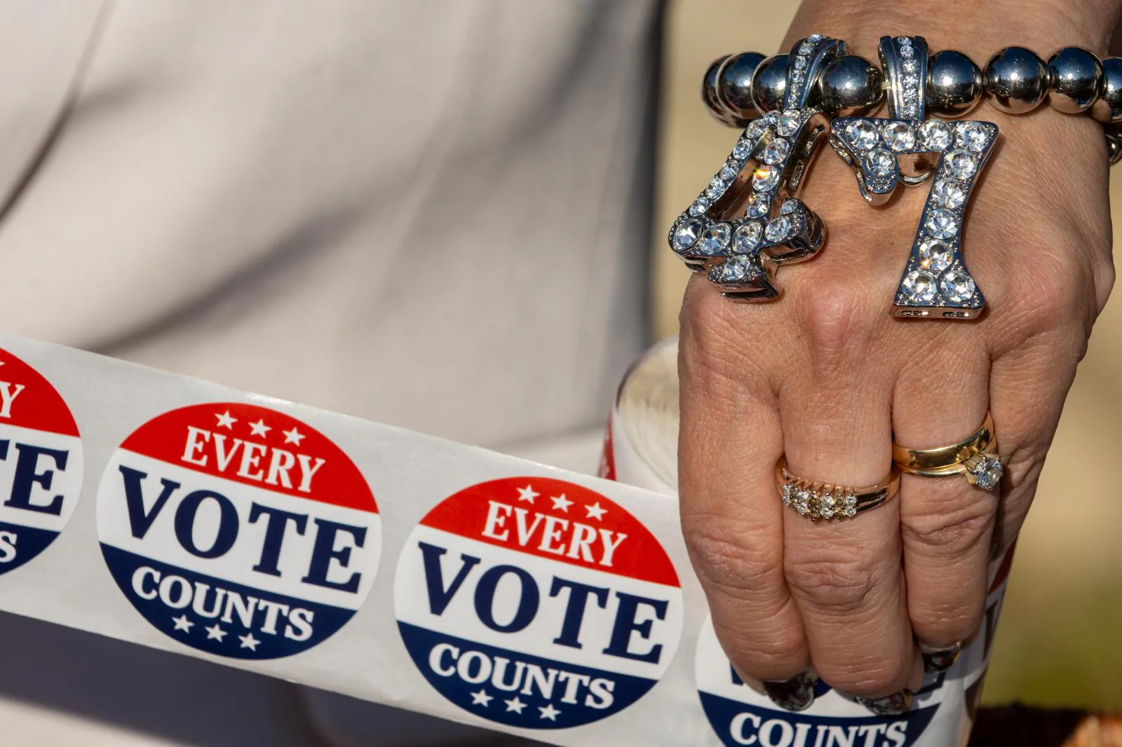 Una seguidora de Trump con una pulsera «47» sostiene pegatinas de «Cada voto cuenta» a las puertas de un colegio electoral 