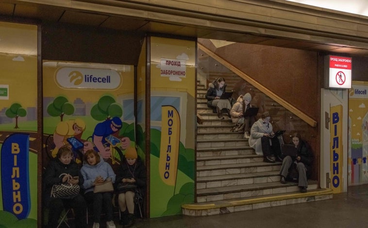 Imagen principal - Una mujer usa su computadora portátil mientras se refugia en una estación de metro durante una alarma de ataque aéreo en Kiev