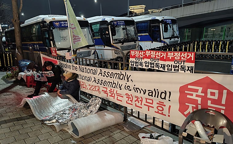 Imagen principal - Una pancarta que llama a «disolver la Asamblea Nacional», un autobús bloquea la residencia del presidente y partidarios de Yoon se manifiestan en los alrededores del edificio