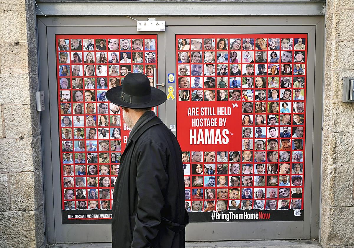 Un hombre camina delante de un cartel con las caras de los rehenes