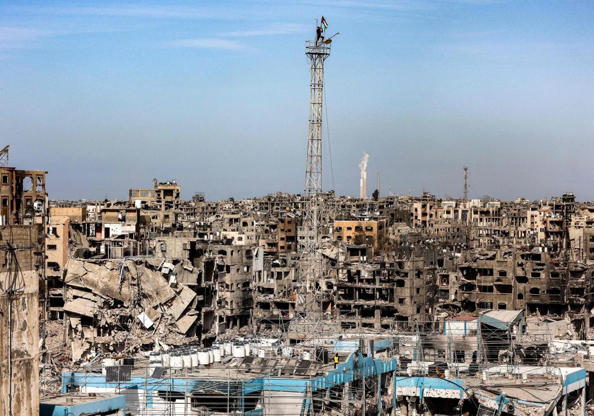 Un hombre coloca una bandera palestina sobre la antena de un edificio destruido