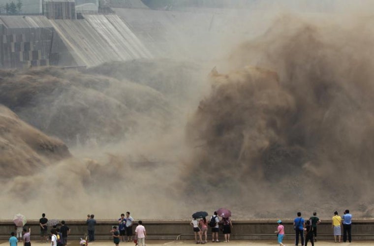 Los residentes locales observan cómo el agua de la inundación cargada de sedimentos brota a través de la presa Xiaolangdi en la provincia de Henan