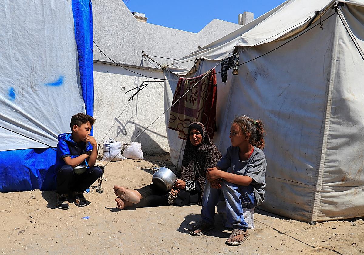 Palestinos desplazados a la Ciudad de Gaza esperan recibir comida de un comedor benéfico con ollas vacías