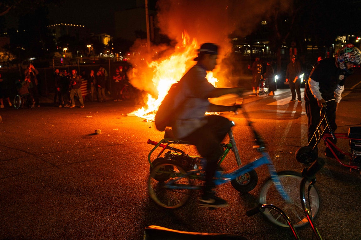 Un ciclista, delante de un vehículo incendiado.