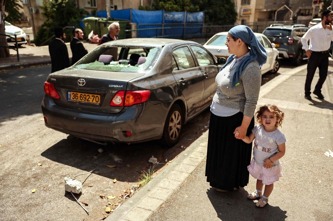 Una madre junto a su hija observa un coche dañado en el lugar de un ataque iraní en la ciudad portuaria israelí de Haifa.