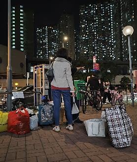Imagen secundaria 2 - En la primera imagen se apilan jaulas para las mascotas cedidas por los vecinos; en la segunda, voluntarias reparten ropa donada para niño; en la última, una vecina de Tai Po abandona el pueblo cargando con sus pertenencias