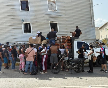 Imagen secundaria 1 - Una mujer descansa en un colchón en plena calle, con los pocos enseres que ha podido rescatar de su casa destruida (primera foto). Un grupo de personas espera para recibir suministros repartidos por voluntarios (segunda foto). Dos mujeres y un niño, con mascarillas, caminan por delante de un mural dedicado a Hugo Chávez (última imagen).