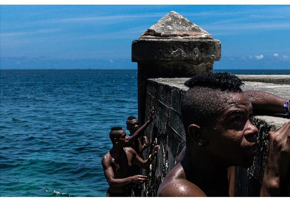 Un grupo de adolescentes se baña en el mar junto al malecón.