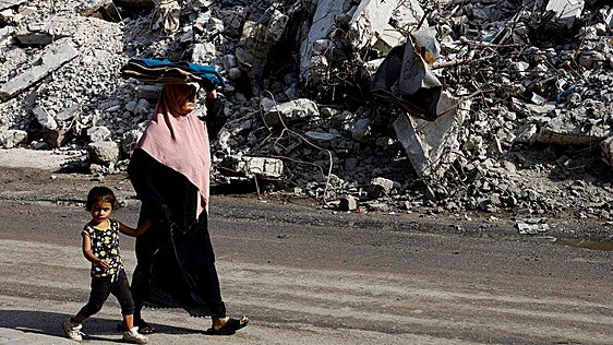 Una mujer y niña gazatíes caminan junto a un edificio derribado.