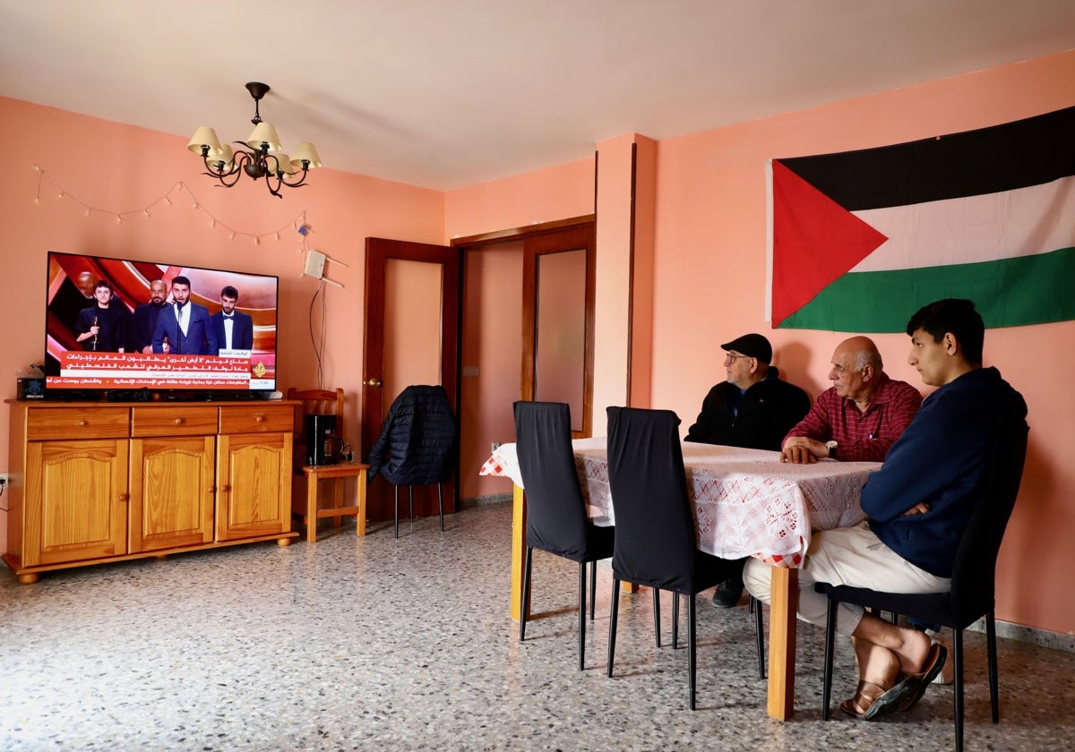 Los gazatíes Riad Ali el Aila, con su hijo, y Salah Awad el Sousi (con gorra) ven en su casa de Pilas (Sevilla) las noticias en Al Yazira sobre el documental palestino ganador del Oscar 'No other land'