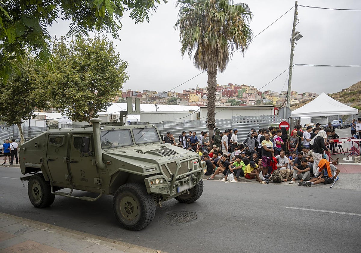 Un blindado militar pasa junto a una cola de inmigrantes, en Ceuta