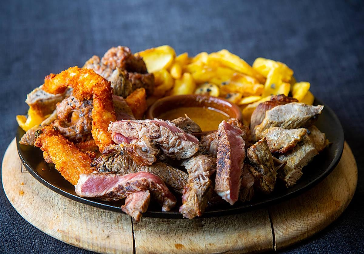 Un plato de carne con salsa, patatas y otros acompañamientos