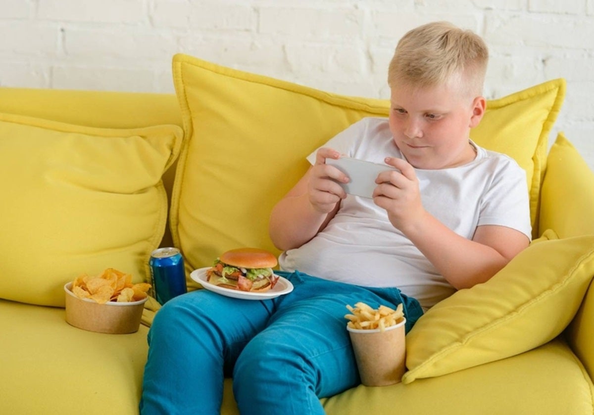 Niño sentado en un sofá comiendo y jugando con el móvil