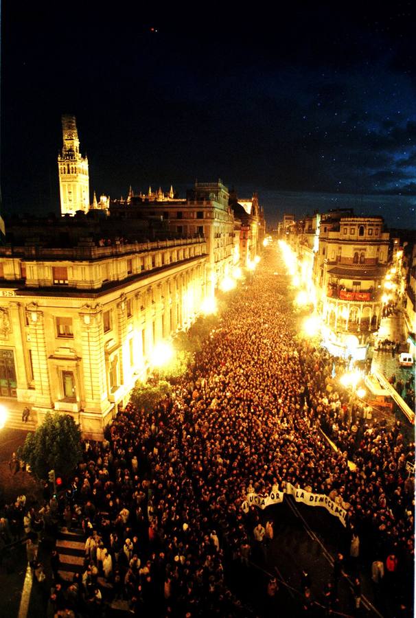 Una imagen nocturna de la cabecera de la manifestación avanzando por la avenida de la Constitución con la Giralda iluminada al fondo. En el Ayuntamiento, la alcaldesa Soledad Becerril leyó una declaración en la que afirmó, entre otras cosas, que "quienes solo saben disparar por la espalda no van a atemorizar a un pueblo fuerte como el nuestro, a una ciudad acogedora y de paz como Sevilla"