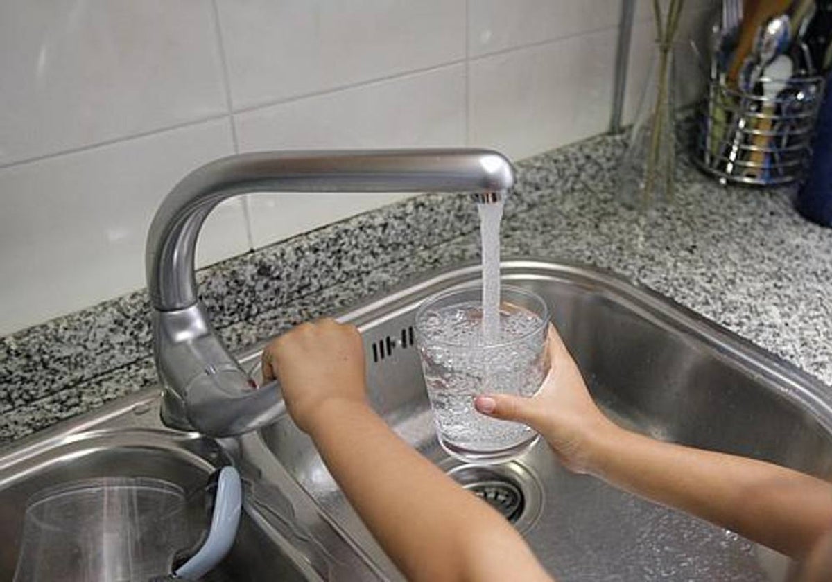 Una persona llena un vaso de agua en un fregadero