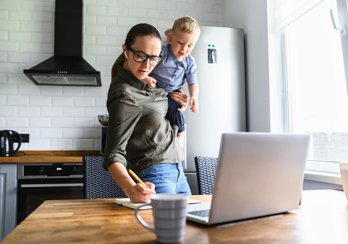 Fotografía de mujer haciendo tareas con su hijo en brazos