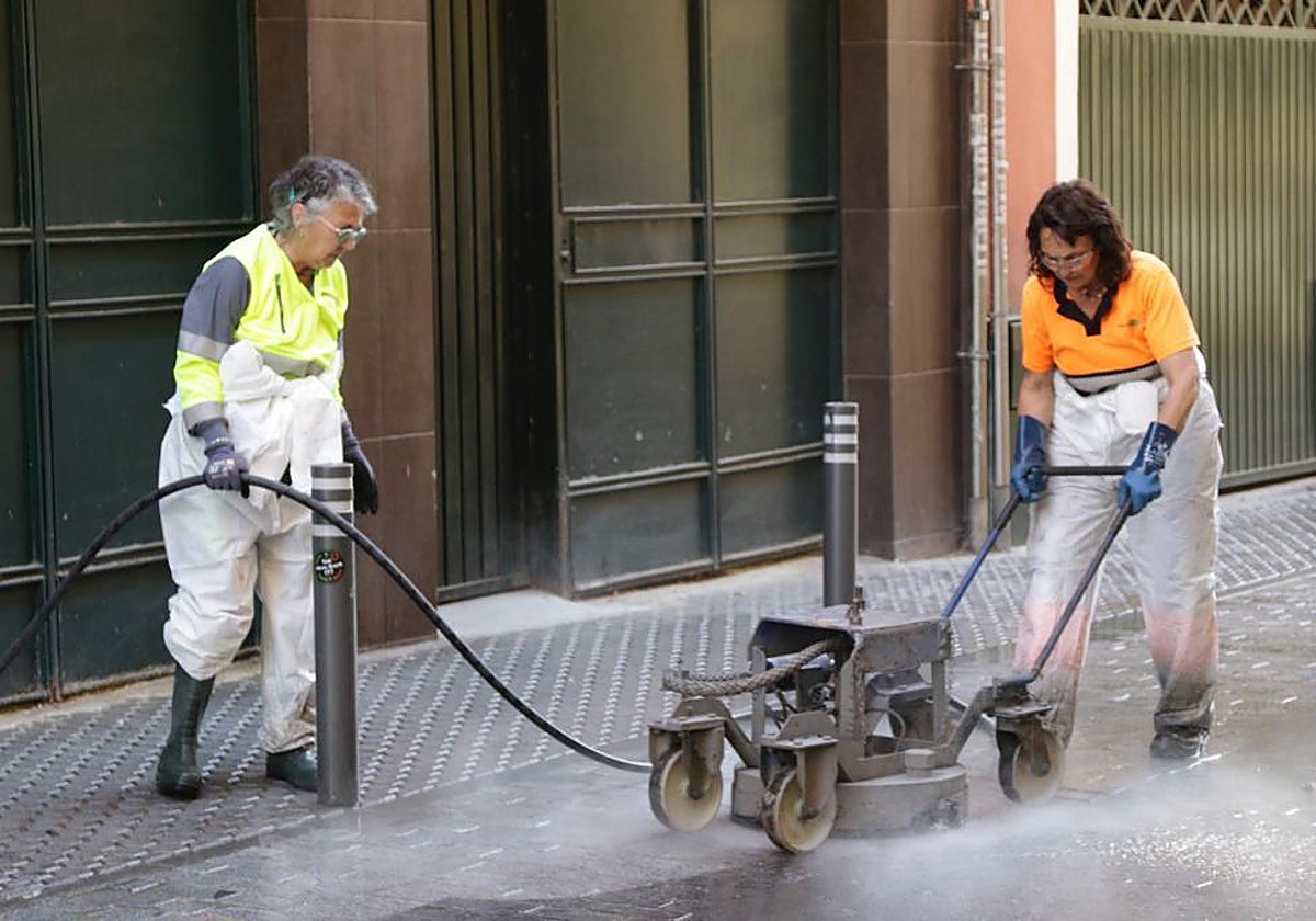 Dos personas trabajan quitando cera en una calle sevillana