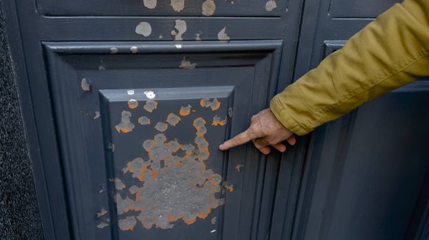 Un vecino señala los restos de impactos en la puerta de una vivienda