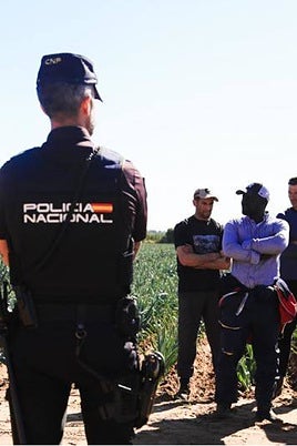 Un agente de Policía delante de un grupo de jornaleros en la finca que están inspeccionando