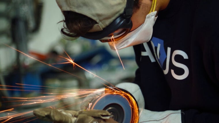 Un estudiante miembro de la escudería ARUS lijando una pieza con una radial para el nuevo coche