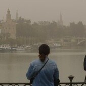 Dos jóvenes fotografían la Torre del Oro de Sevilla con el cielo cubierto por una intensa calima