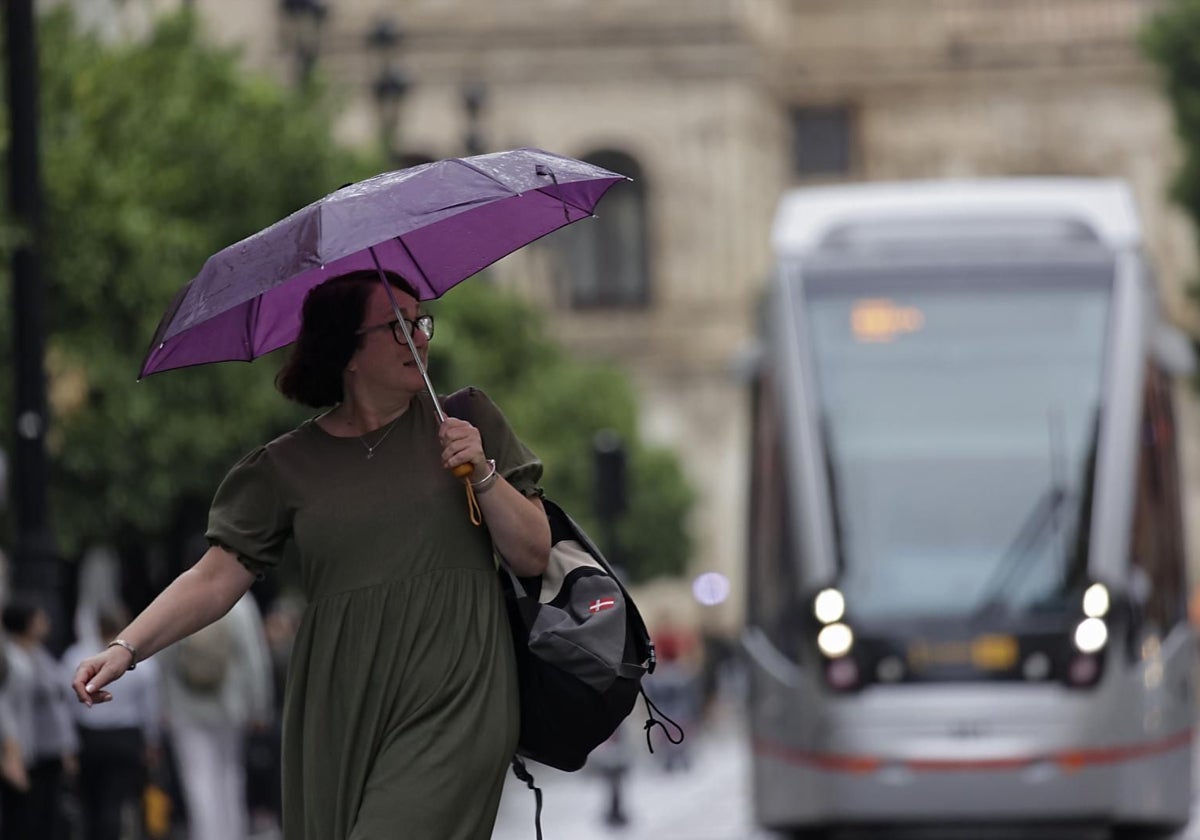 Una mujer camina bajo la lluvia por el Centro, con el tranvía al fondo