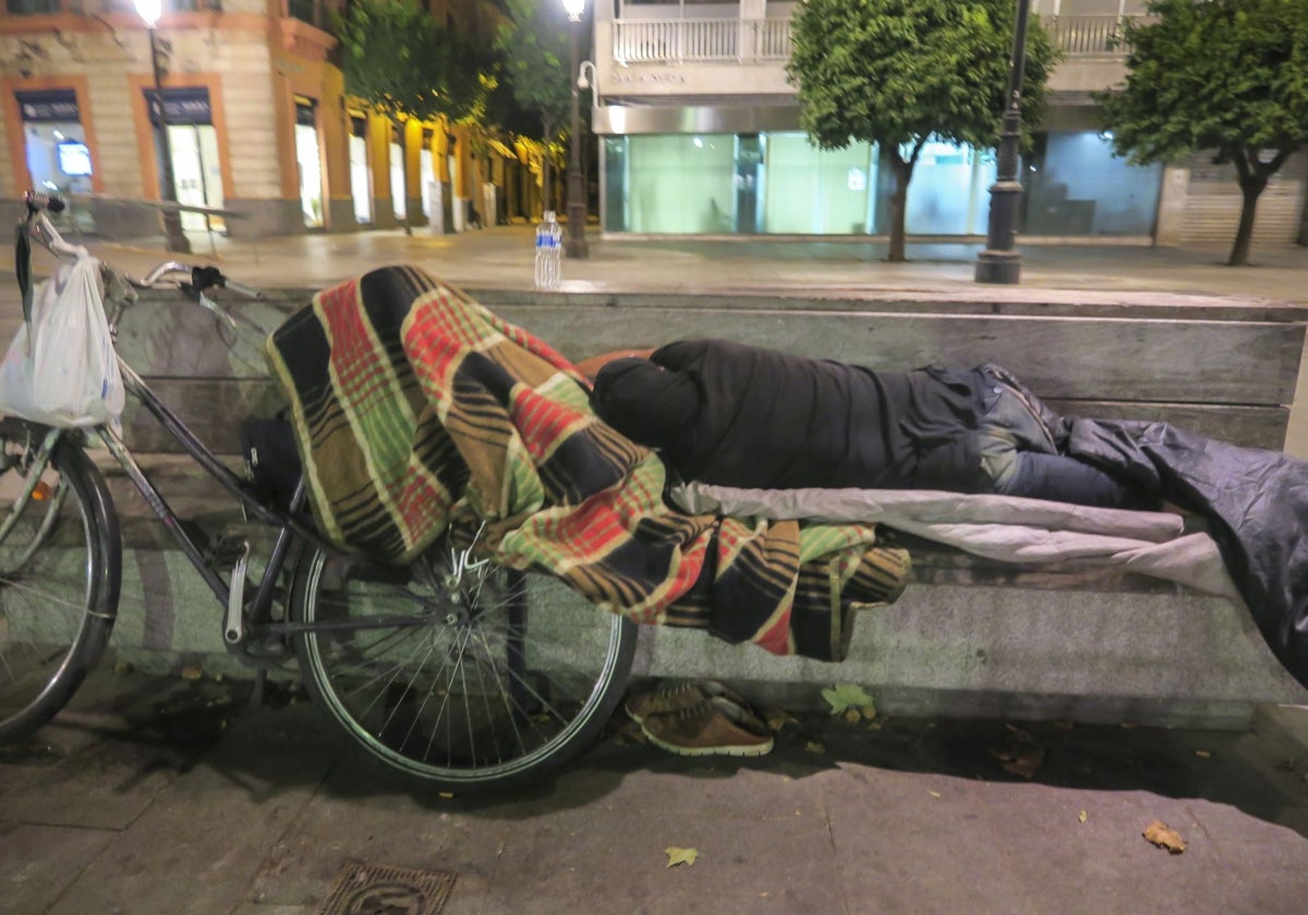 Una persona sin hogar pernocando en un banco de la Plaza Nueva