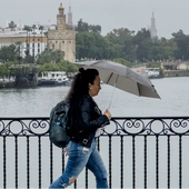 Una mujer camina bajo la lluvia en Sevilla, por el Puente de Triana
