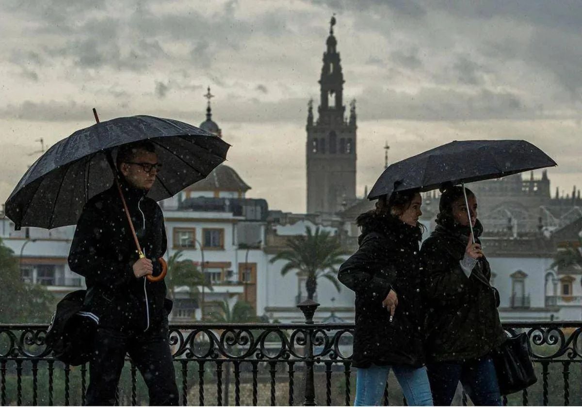 Personas caminando con paraguas bajo la lluvia por el Puente de Triana