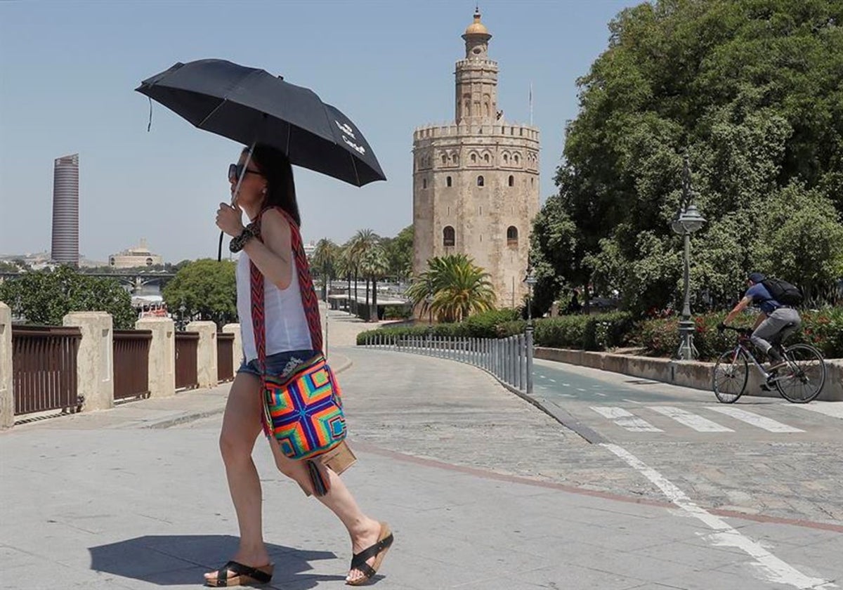 Una mujer se cubre con un paraguas durante un día de calor en Sevilla, mientras camina junto a la Torre del Oro
