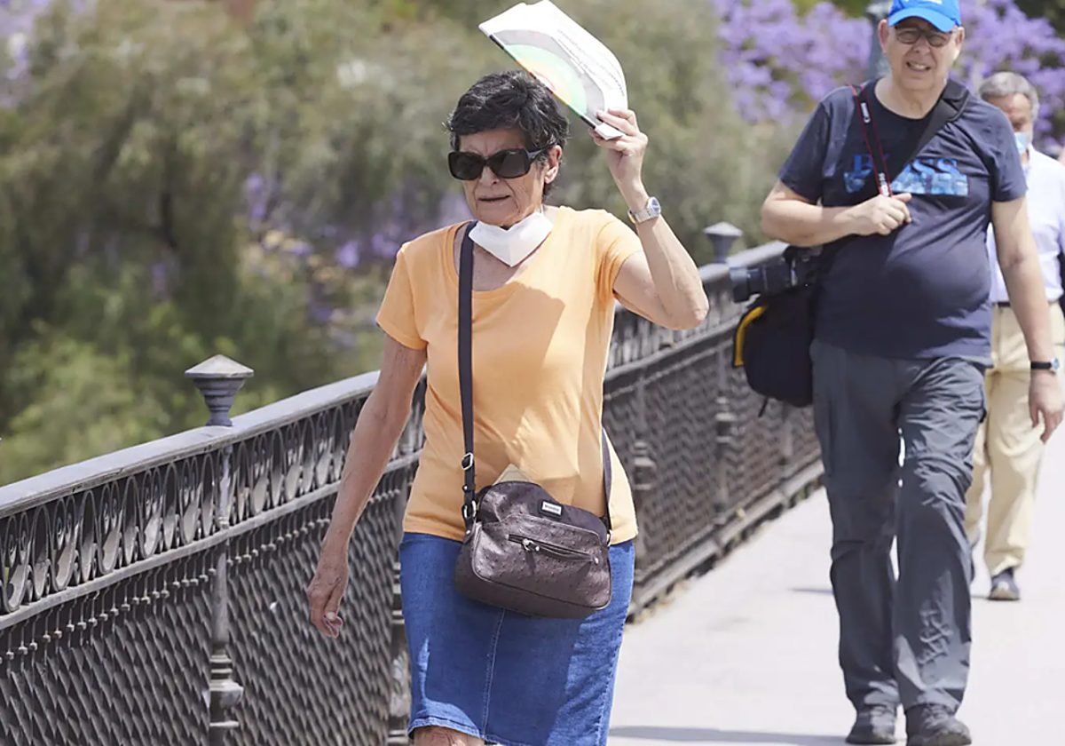 Una mujer se protege del calor mientras pasea por el Puente de Triana