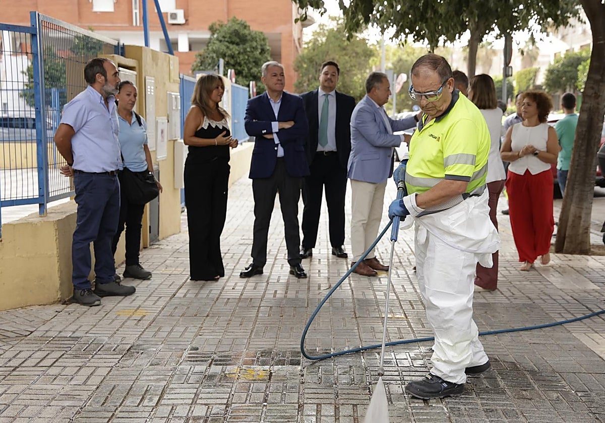 Un operario de Lipasam trabajando en la puerta del CEIP Isbilya ante la mirada del alcalde
