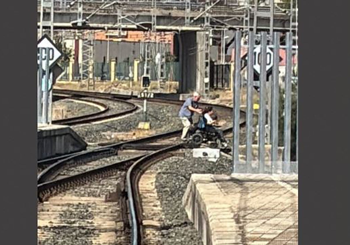 Una viajera con movilidad reducida es ayudada a cruzar por las vías en la estación de tren de Utrera