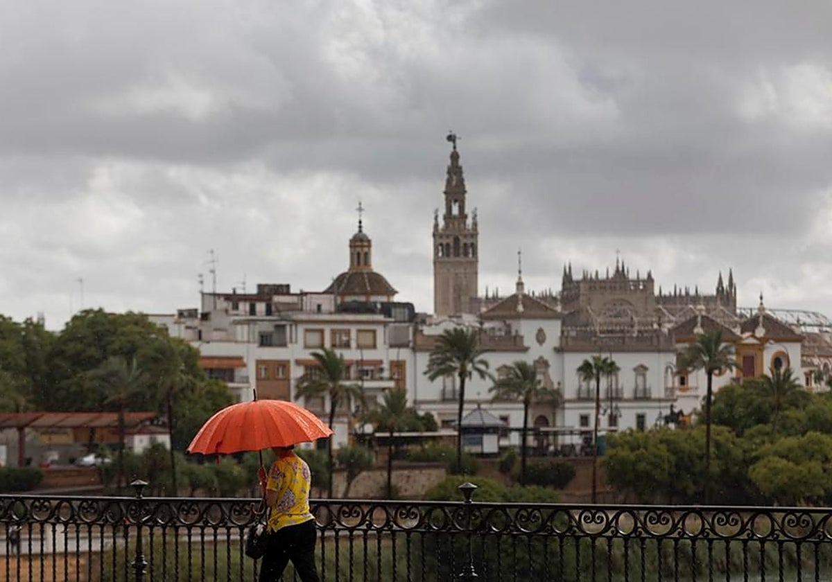 Una mujer camina por el puente de Triana cubriéndose con un paraguas durante un día de inestabilidad en Sevilla